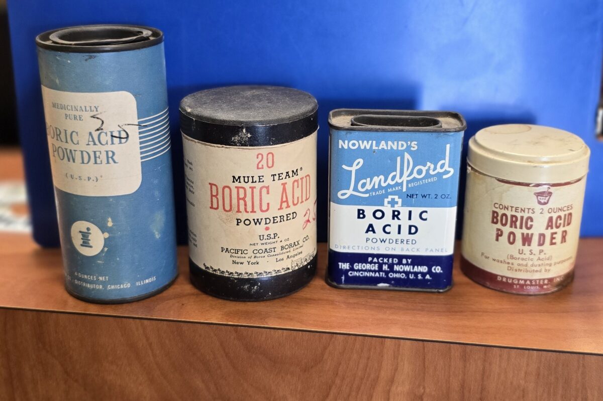 Group of vintage boric acid containers including metal tins and cardboard tubes from early 20th century pharmacies.