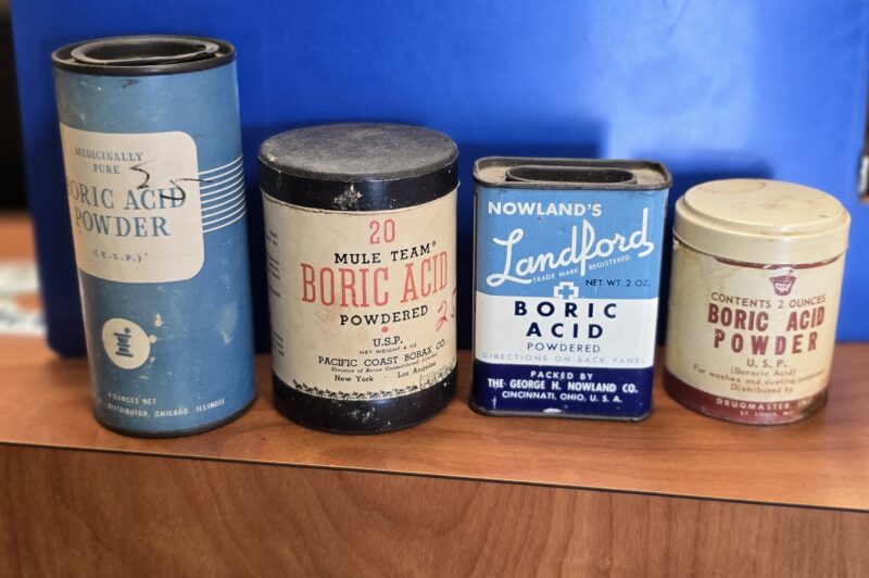 Group of vintage boric acid containers including metal tins and cardboard tubes from early 20th century pharmacies.