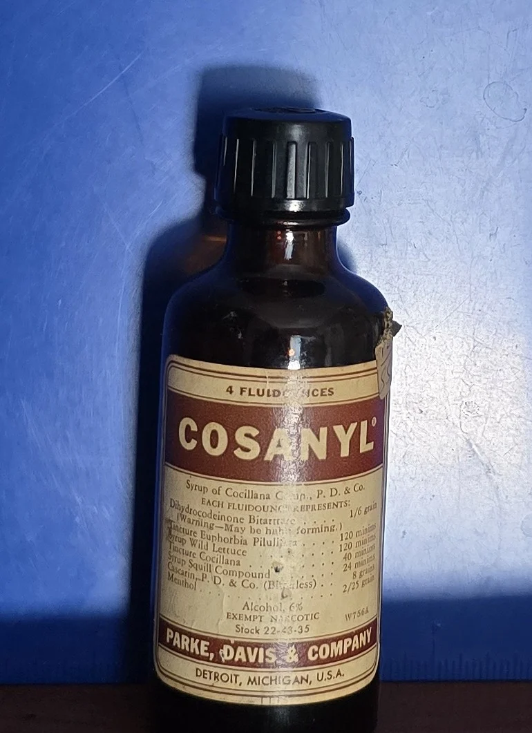 Vintage Cosanyl cough syrup bottle with label showing narcotic and botanical ingredients.