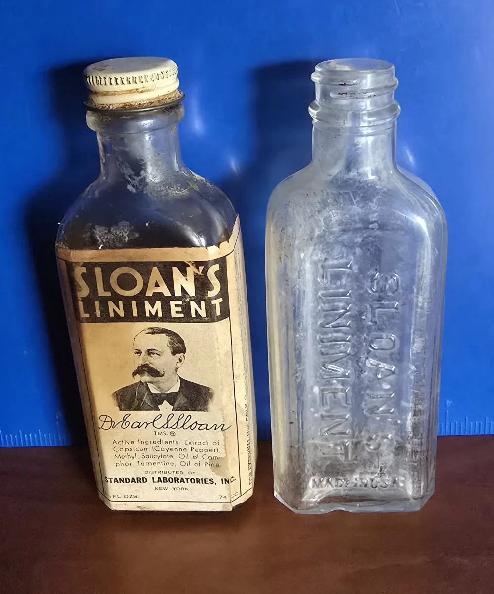 Two vintage Sloan’s Liniment bottles side-by-side; one with intact label and cap, one clear embossed ‘SLOAN’S LINIMENT’ bottle, against a blue backdrop.