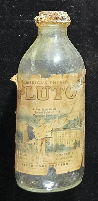 Antique Pluto Water glass bottle with partially intact label and mineral-stained stopper, marketed as a powerful laxative from French Lick, Indiana.
