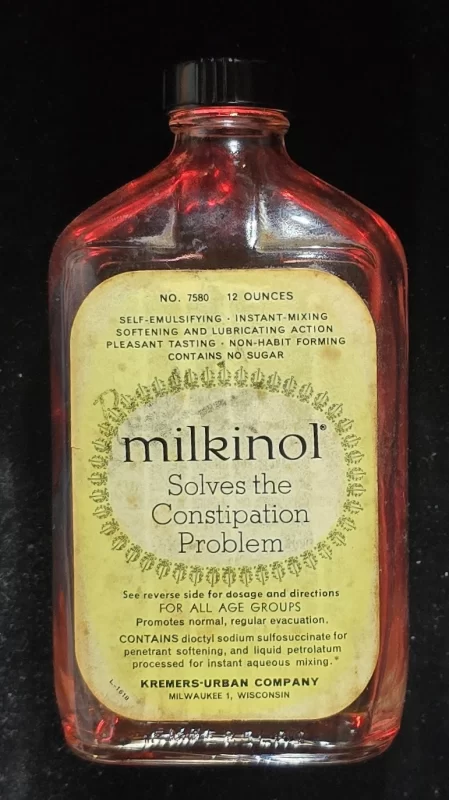 Flat amber Milkinol bottle with yellow label and black cap advertising constipation relief and softening action; produced by Kremers-Urban Company.