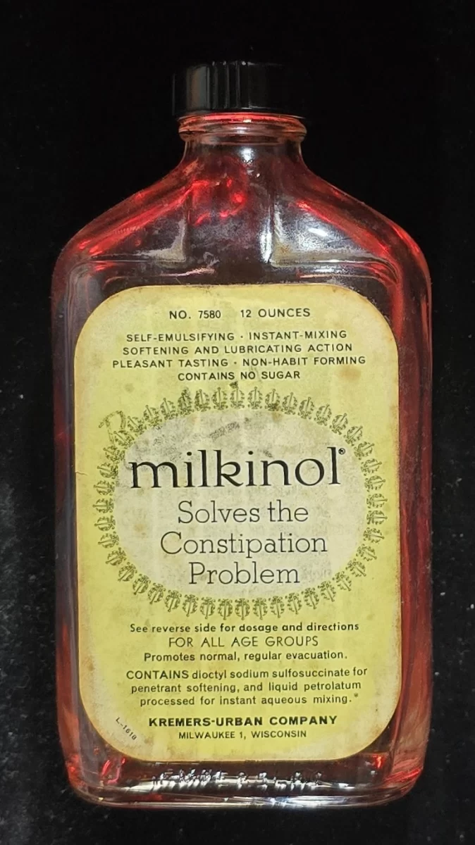 Flat amber Milkinol bottle with yellow label and black cap advertising constipation relief and softening action; produced by Kremers-Urban Company.