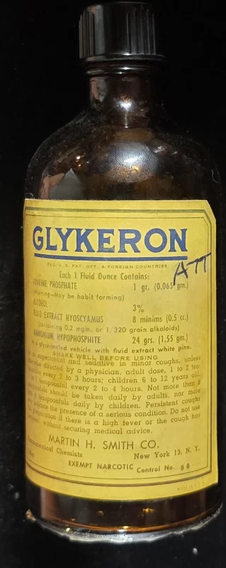 Front view of antique Glykeron bottle with bright yellow label listing codeine, hyoscyamus, and alcohol content; manufactured by Martin H. Smith Co., New York, NY.