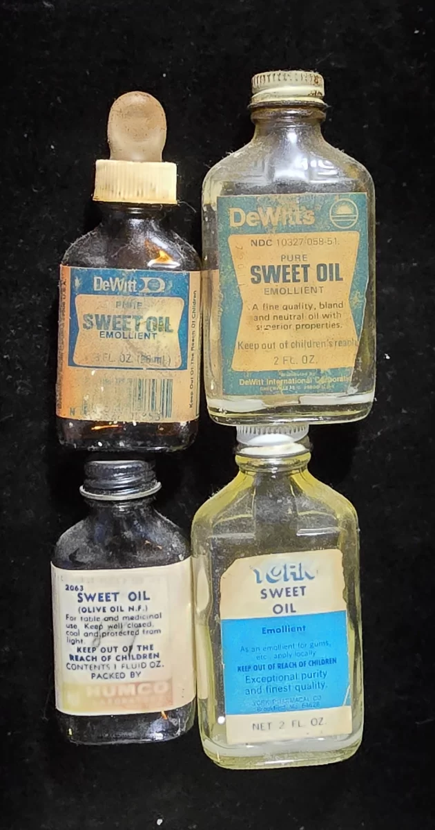 Four vintage Sweet Oil bottles from DeWitt, York, and Humco brands, showcasing various sizes, label styles, and glass tints.