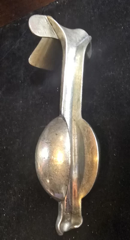 Vintage weighted vaginal speculum with bulbous counterweight and flared insertion blade, shown on dark background