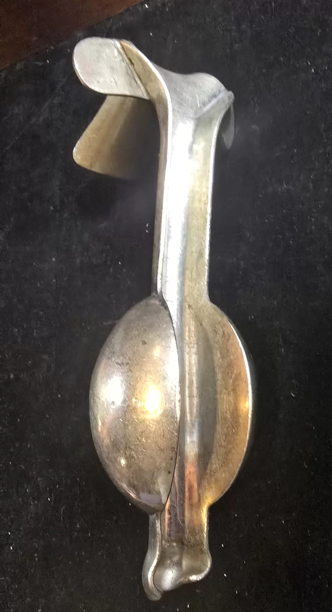 Vintage weighted vaginal speculum with bulbous counterweight and flared insertion blade, shown on dark background