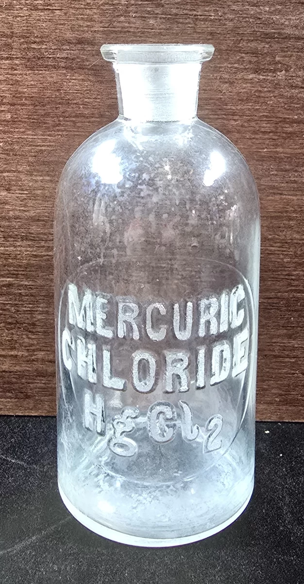Clear antique apothecary bottle labeled “Mercuric Chloride HgCl₂,” no stopper present