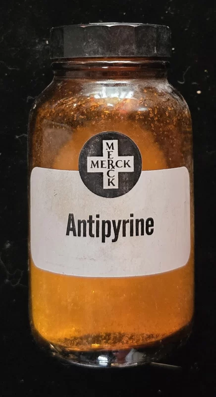 Merck Antipyrine amber glass bottle with black screw cap and original labels, vintage pharmaceutical container.