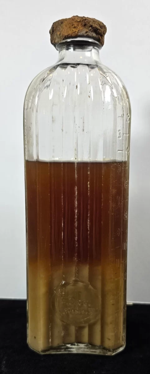 Antique Universal Embalming Fluid bottle with contents, embossed glass, cork top, and sediment.