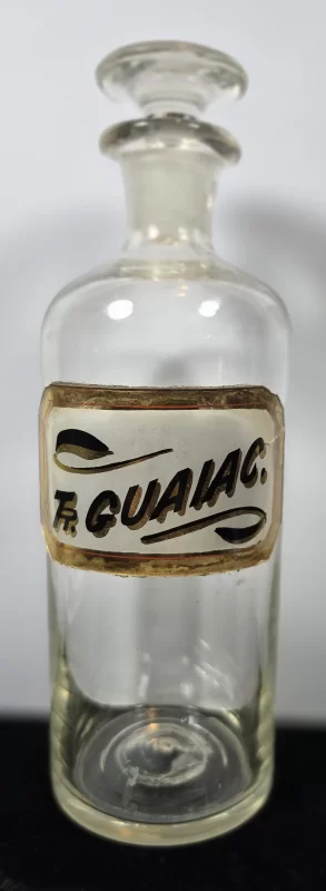 Clear glass apothecary bottle with enameled label reading Fr. Guaïac. and ground glass stopper.