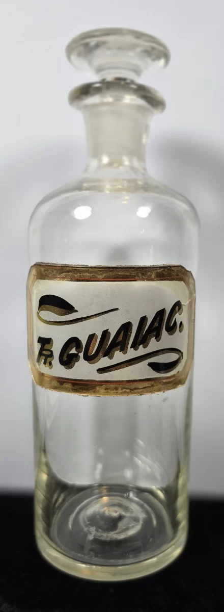 Clear glass apothecary bottle with enameled label reading Fr. Guaïac. and ground glass stopper.