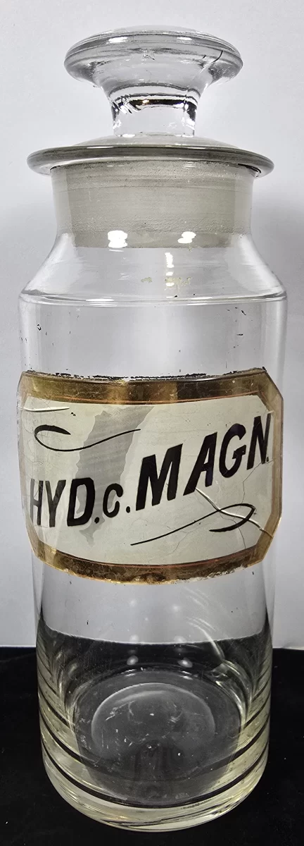 Large antique apothecary jar labeled HYD c MAGN with glass stopper, clear glass pharmacy container.