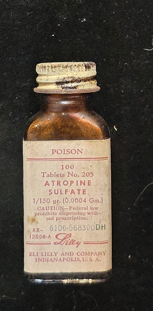 Small amber glass bottle labeled “Atropine Sulfate, 1/150 grain, 100 tablets, No. 205” by Eli Lilly & Company, Indianapolis. White label with red “POISON” warning and Lilly script logo.