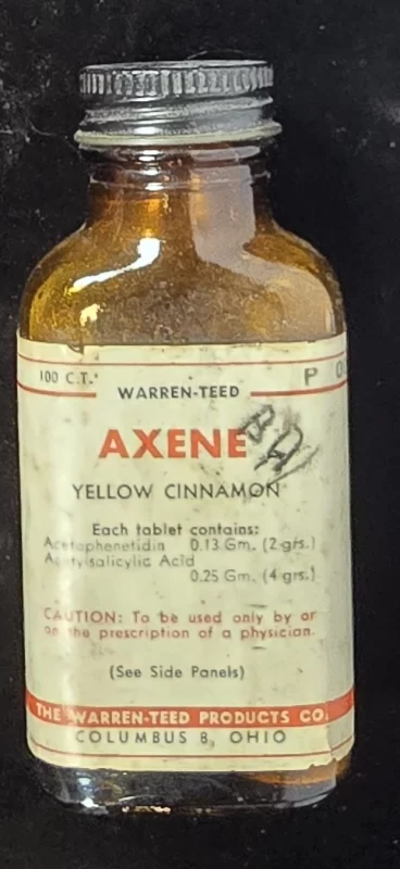 Amber glass bottle labeled “Axene – Yellow Cinnamon,” showing acetophenetidin and acetylsalicylic acid contents.