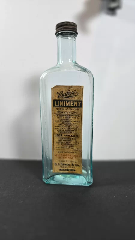 Aqua glass bottle of Baker’s Liniment by S.F. Baker & Co., Keokuk, Iowa, with original label and metal cap.