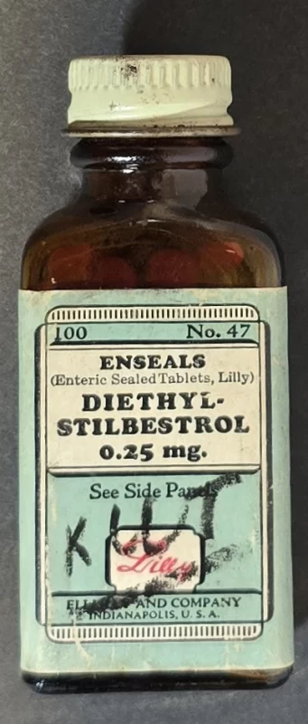Amber glass bottle of Eli Lilly Diethylstilbestrol Enseals 0.25 mg with green warning label and red tablets inside.