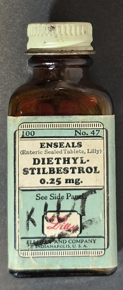Amber glass bottle of Eli Lilly Diethylstilbestrol Enseals 0.25 mg with green warning label and red tablets inside.