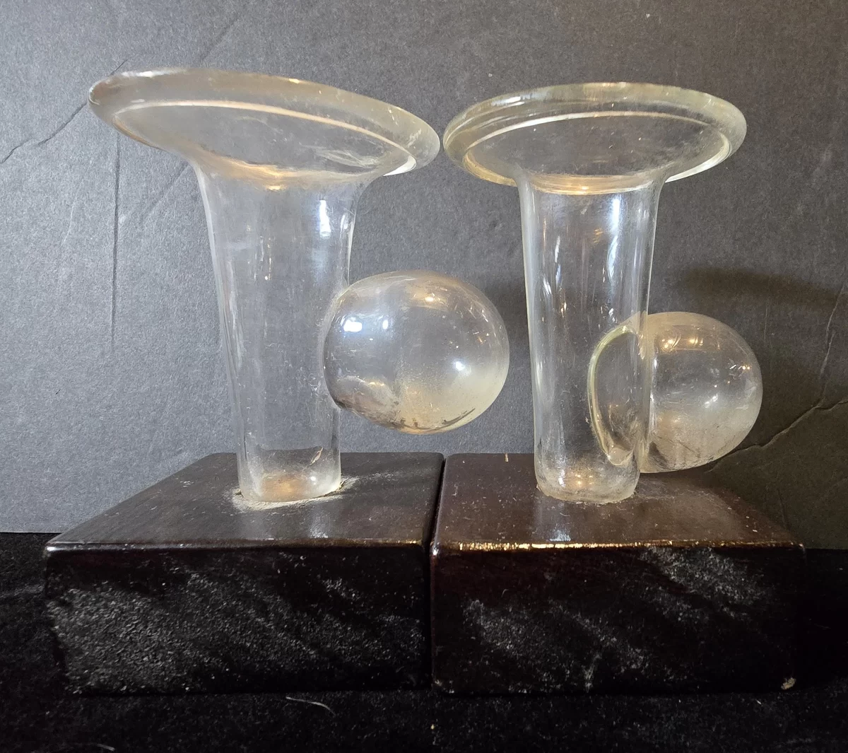 Pair of clear hand-blown glass breast pump cups with suction bulbs mounted on wooden bases, early medical lactation devices.