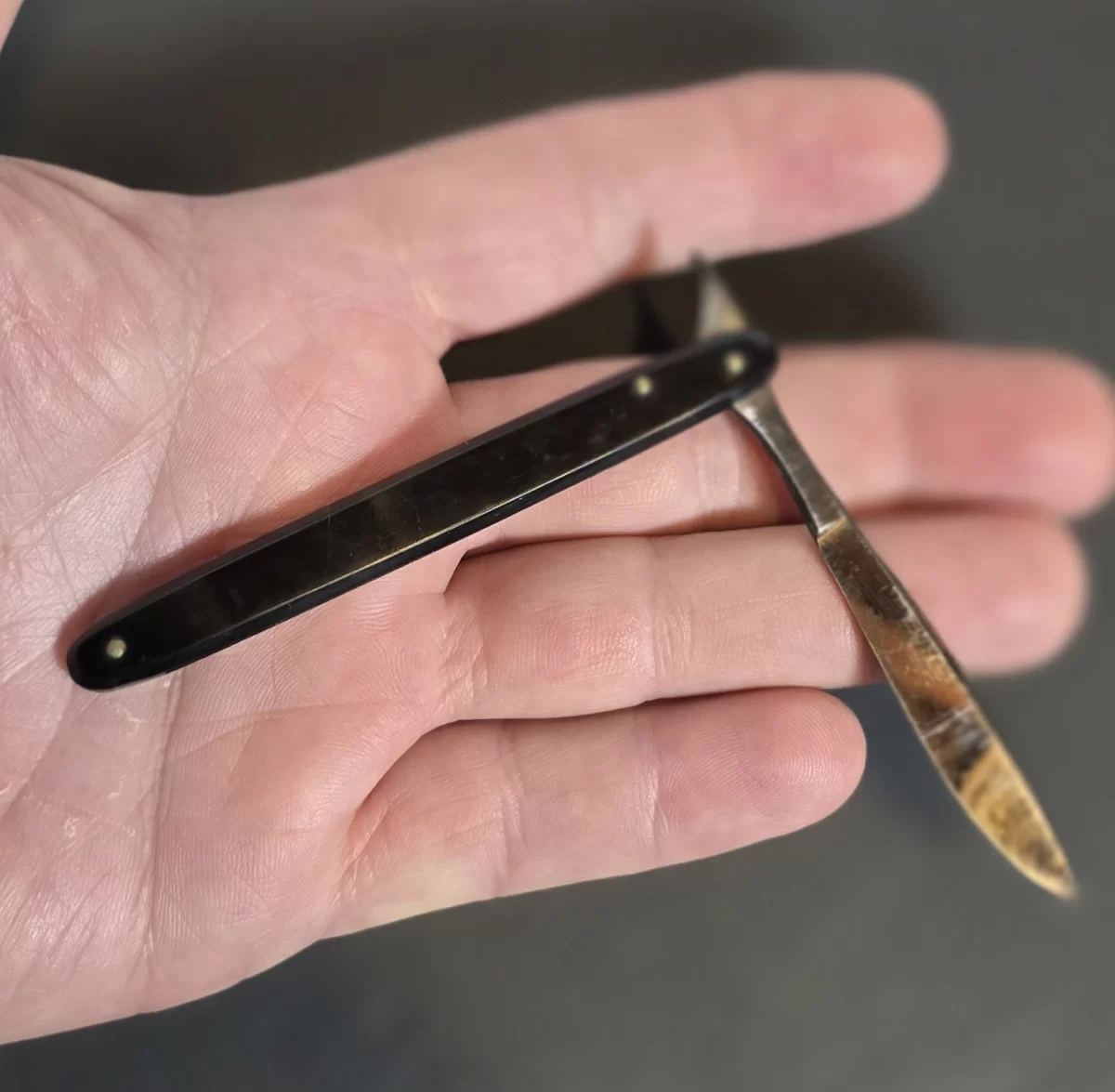 antique surgical thumb lancet with black handle and folding steel blade.