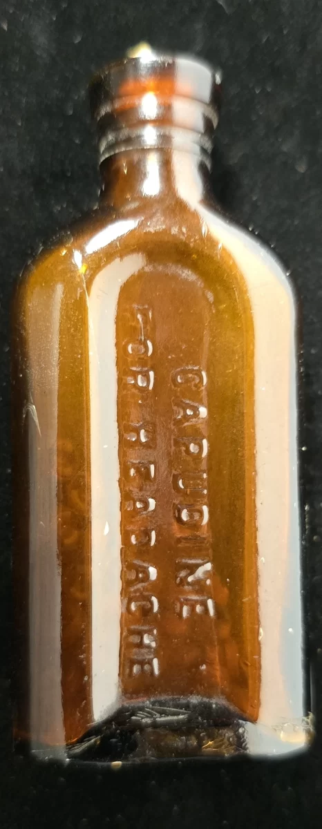 Small amber embossed bottle reading ‘Capudine For Headache’ with screw-thread top and dried residue.