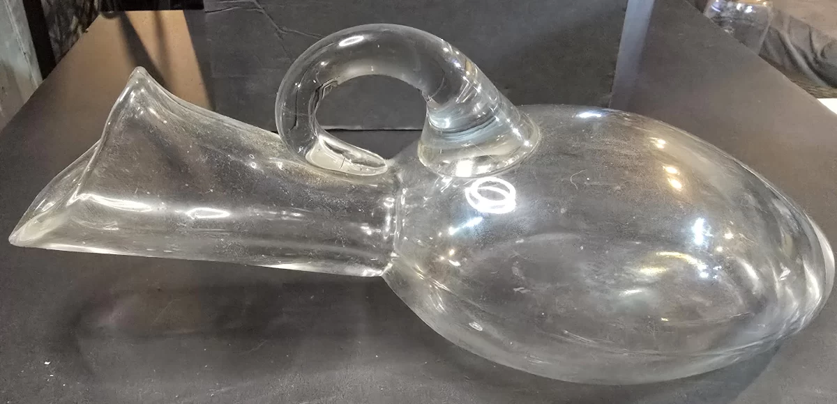 Clear glass female bedside urinal with oval mouthpiece and loop handle, c. 1930–1950