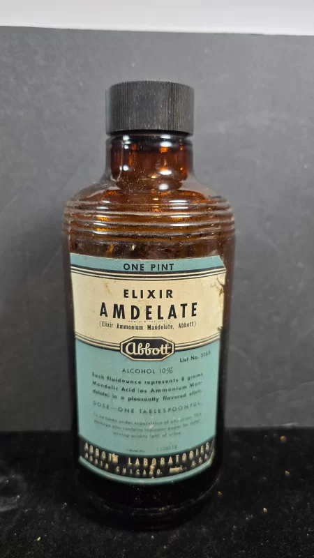 Amber glass bottle of Abbott Elixir Amdelate with original screw cap and blue pharmaceutical label, early urinary antiseptic.