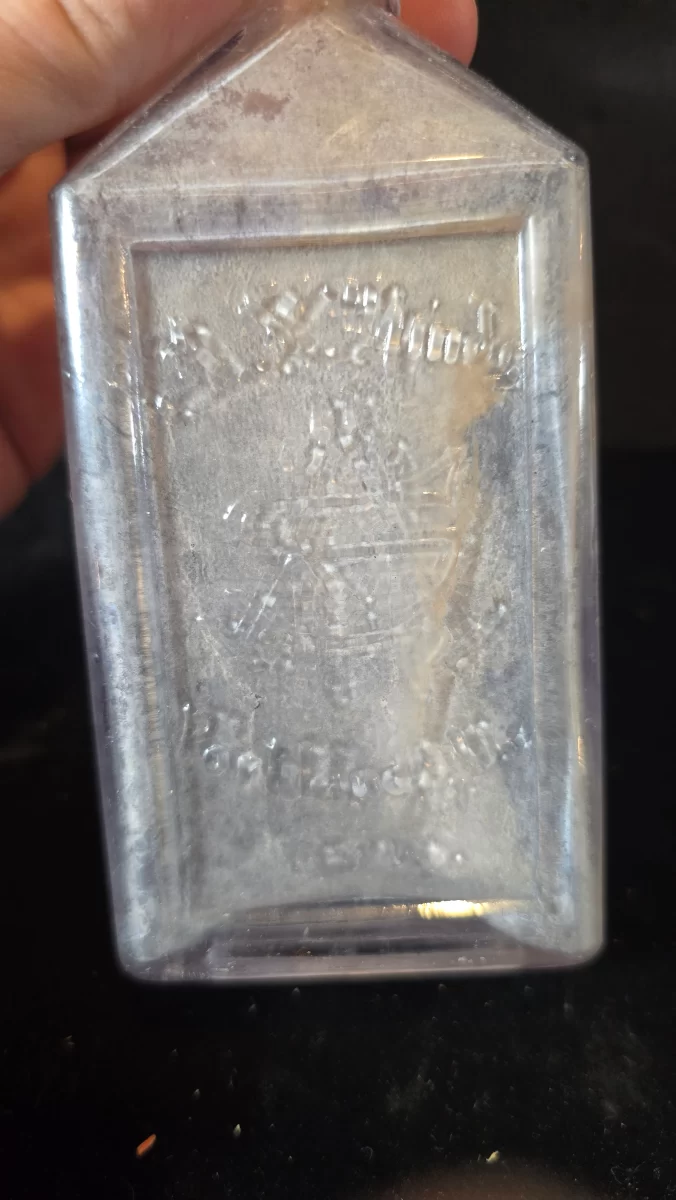 Clear rectangular apothecary bottle embossed “A. Y. Hinde,” showing sloped shoulders, flared lip, and heavy internal residue from historical pharmaceutical use.