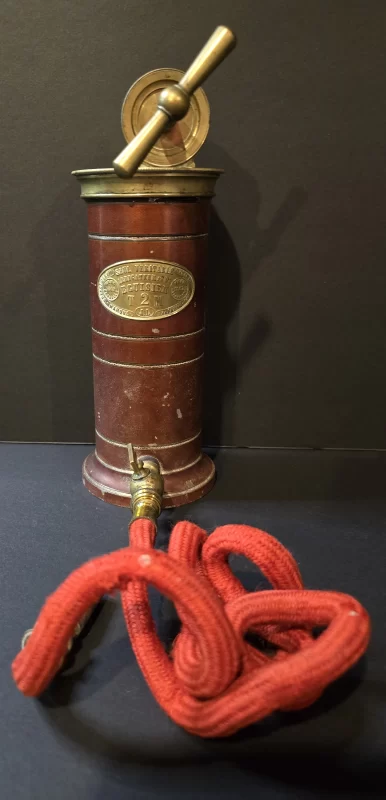 Eguisier T2M irrigator with red cylindrical body, brass valve mechanism, and original cloth hose